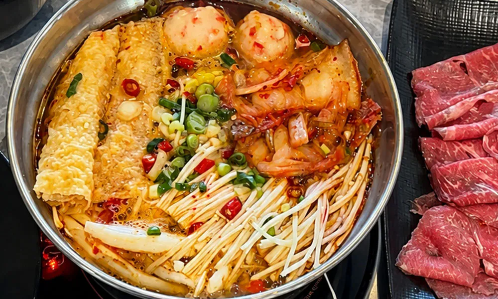 Spicy kimchi hot pot loaded with enoki, tofu rolls, meatballs and fresh garnishes at FirePot Korean BBQ & Hot Pot, an Asian Restaurant in Grand Forks