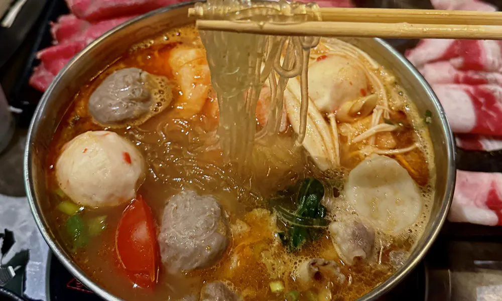 Brothy hot pot with shrimp, beef balls and glass noodles lifted by wooden chopsticks at FirePot Korean BBQ & Hot Pot, an Asian Restaurant in Grand Forks
