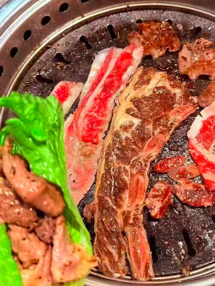 Marbled beef slices grilling on metal barbecue grill plate at FirePot Korean BBQ & Hot Pot, an Asian Restaurant in Grand Forks